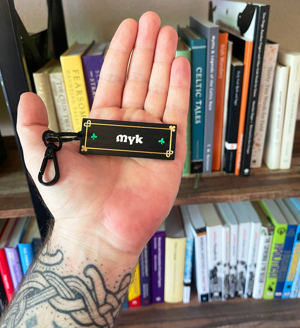 Hand holding a 'myk' keychain in front of a bookshelf